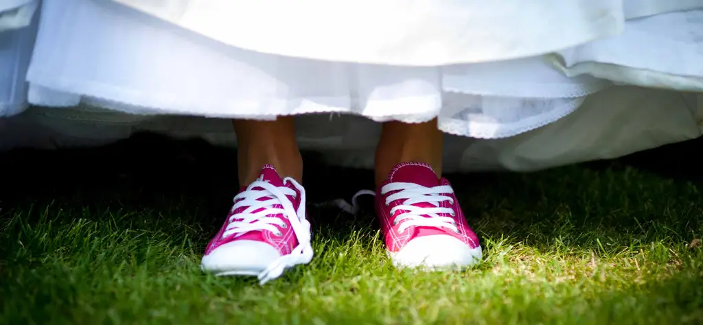 Červené tenisky jako svatební boty pro nevěstu vykukují zpod bílé sukně.